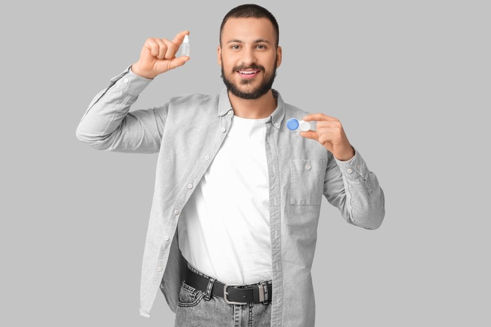 Young,Man,Holding,Eye,Drops,And,Contact,Lenses,On,Grey