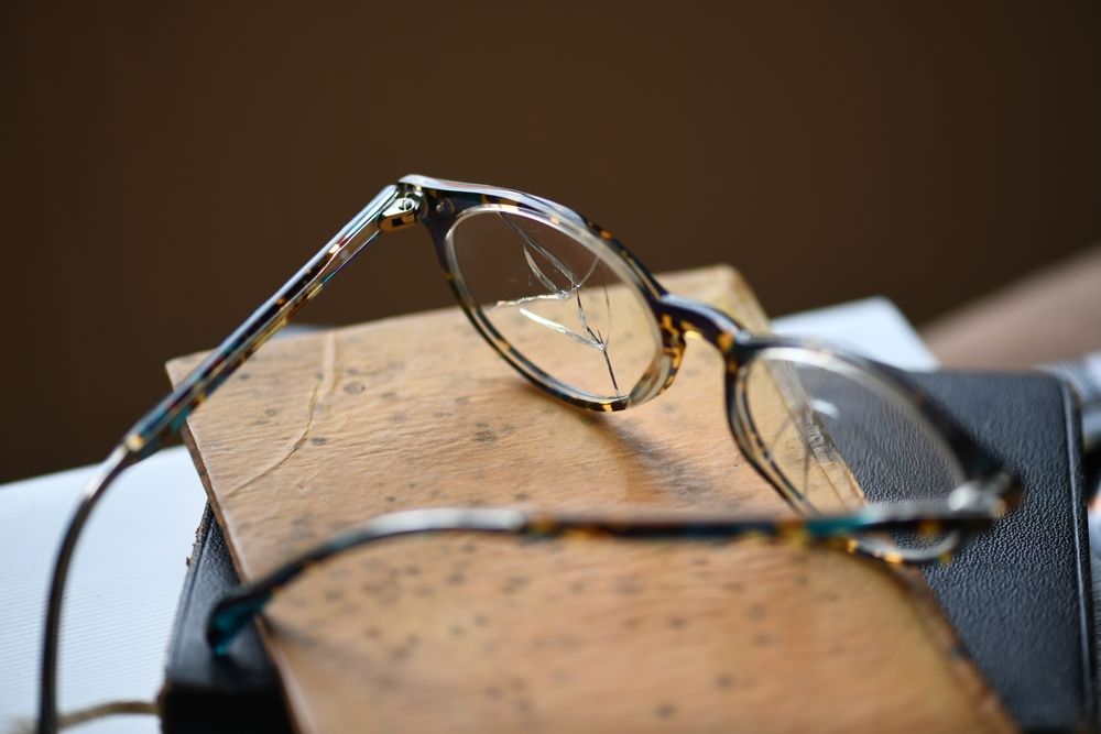 A close-up shot of a pair of broken eyeglasses with cracked lens resting on an aged leather notebook