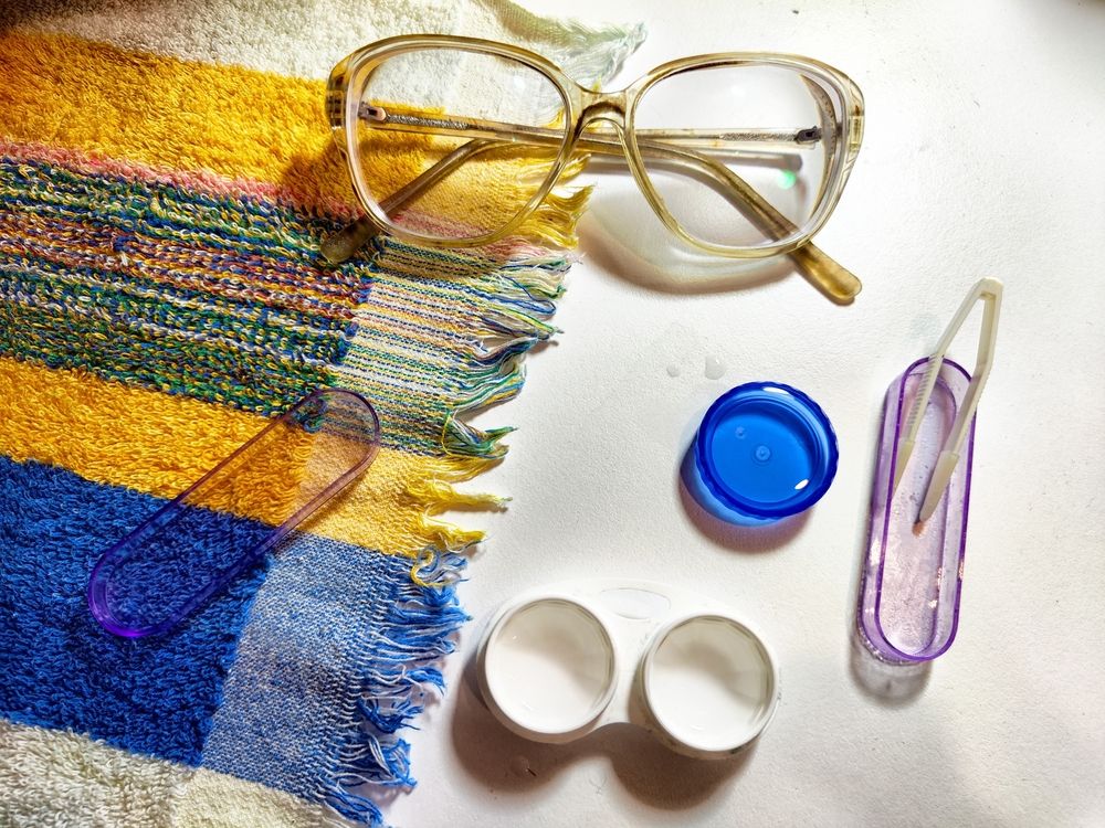 Contact lens case, tweezers, and solution arranged on a vibrant towel, highlighting the importance of eye health and care.