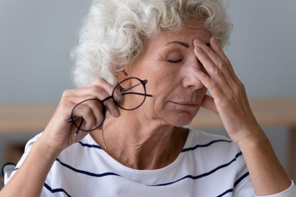 Exhausted mature woman take off glasses suffer from blurry vision or dizziness, have high blood pressure,