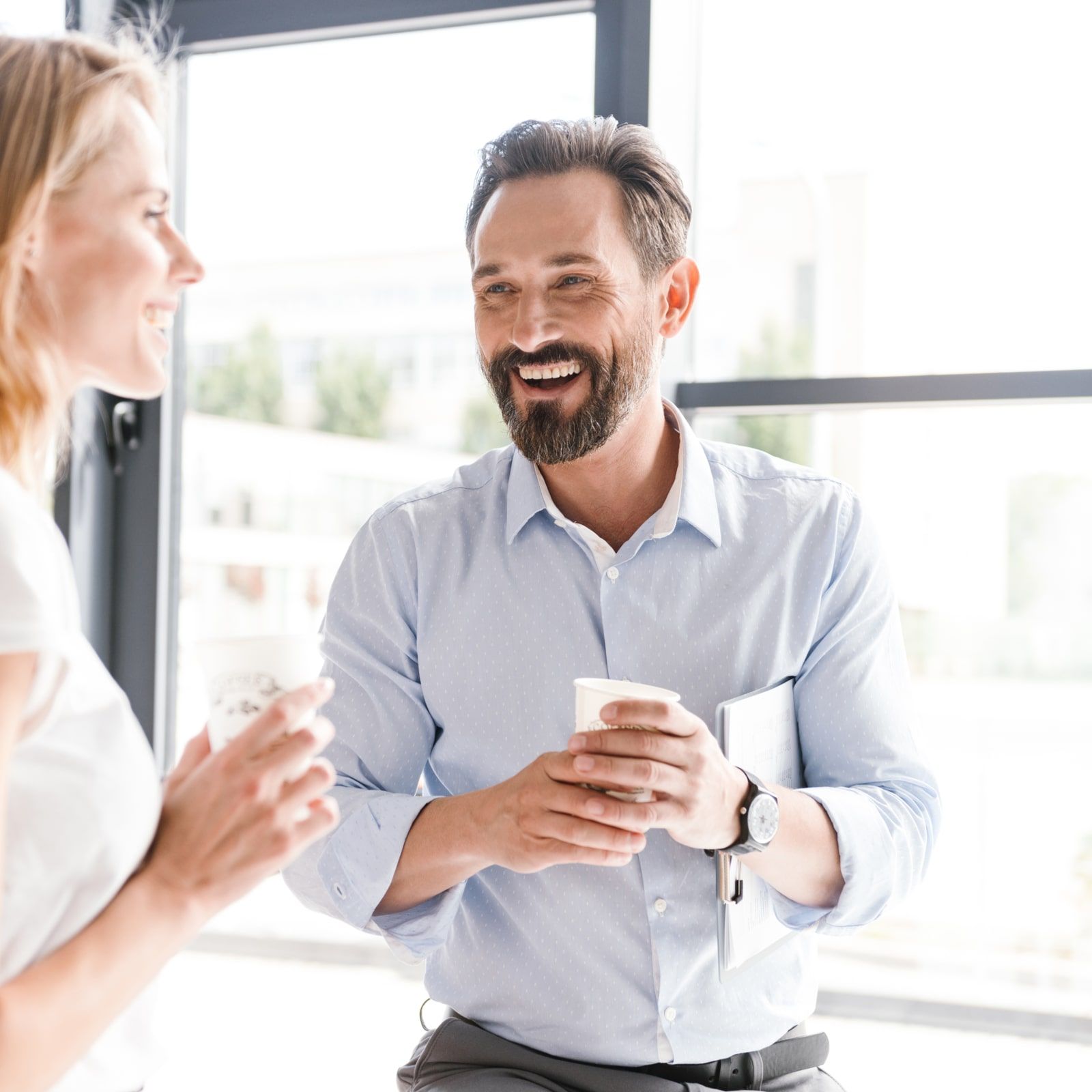 cheerful colleagues talking while standing at the office window