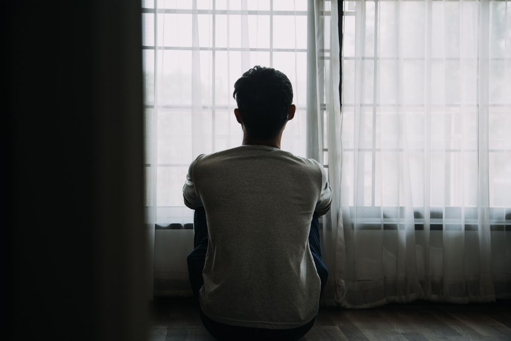 Alone man silhouette staring at the window closed with curtains in bedroom. Man stands at window alone