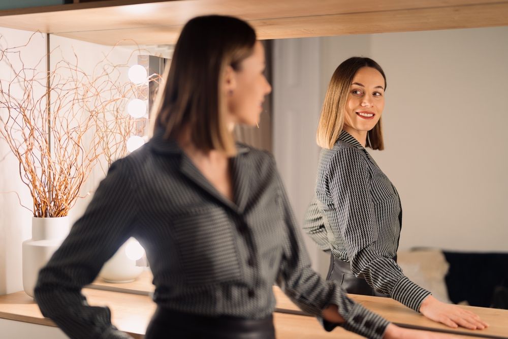 Self-confident Woman looking at her reflection into the mirror indoors. Beautiful interior design