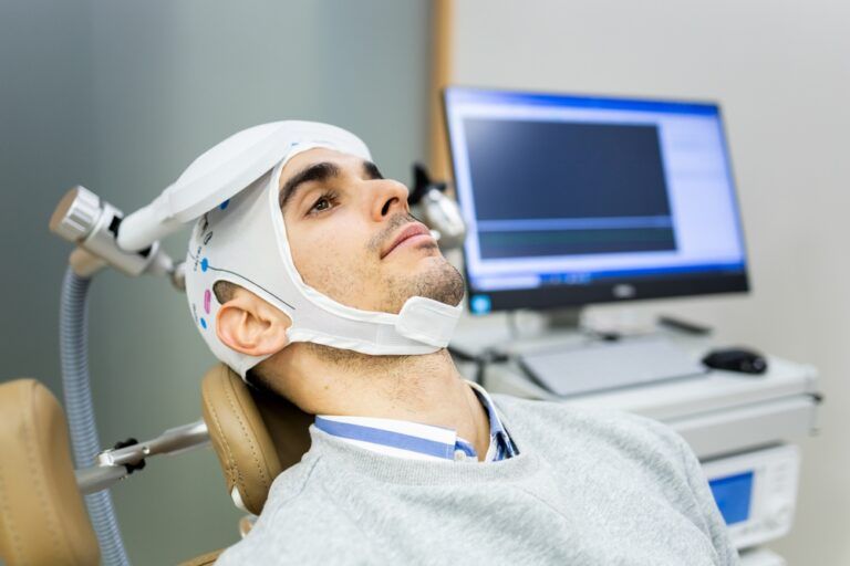 A man in his 30s or 40s undergoes transcranial magnetic stimulation therapy in a psychiatric clinic