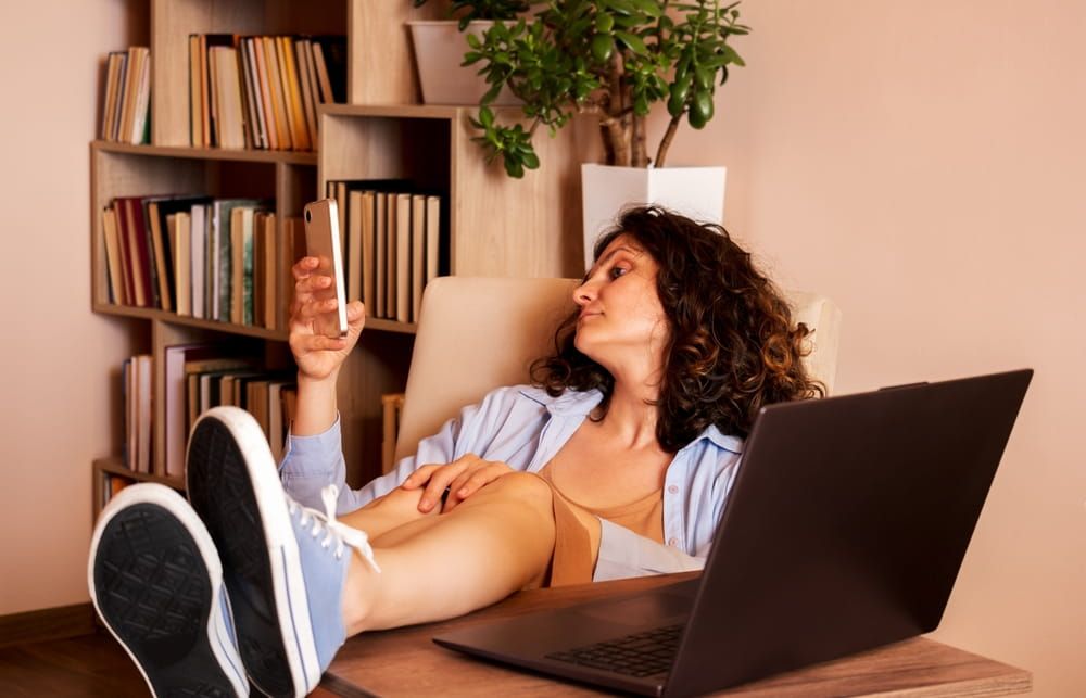 Bored woman with her feet on the desk uses smartphone