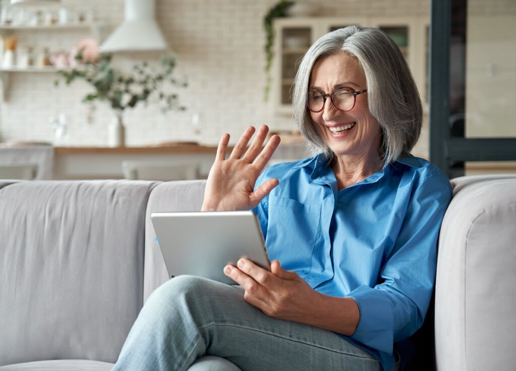 middle aged adult woman waving hand holding digital tablet computer