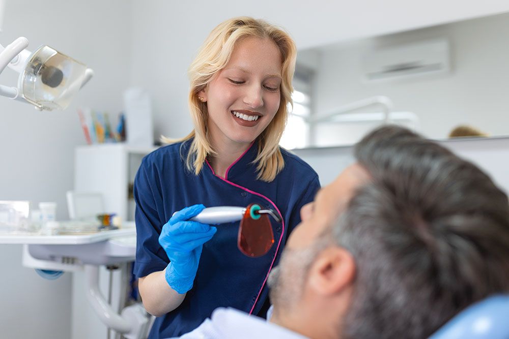 Close up view of man undergoing laser tooth whitening treatment to remove stains and discoloration. Bleaching of the teeth at dentist clinic.