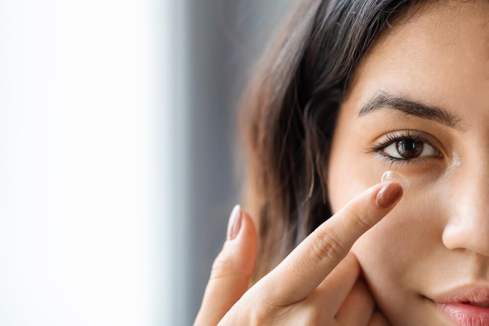 Young woman putting contact lens in her eye at home