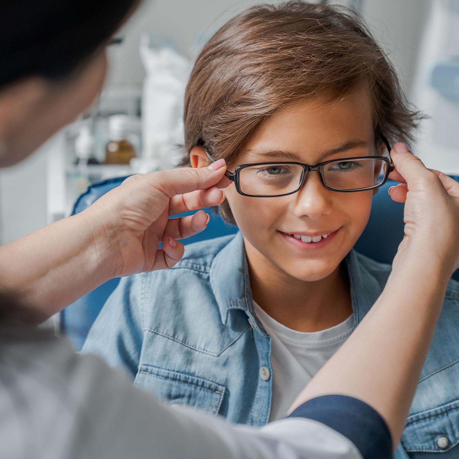 Female doctor putting glasses on little boy in clinic