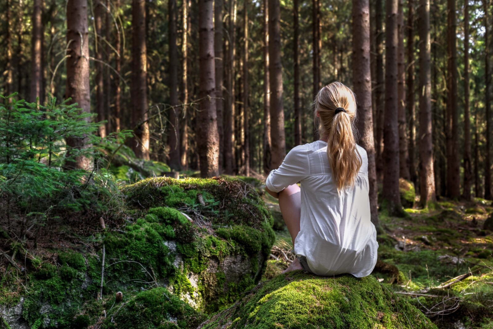 Woman sitting in green forest enjoys the silence and beauty of nature