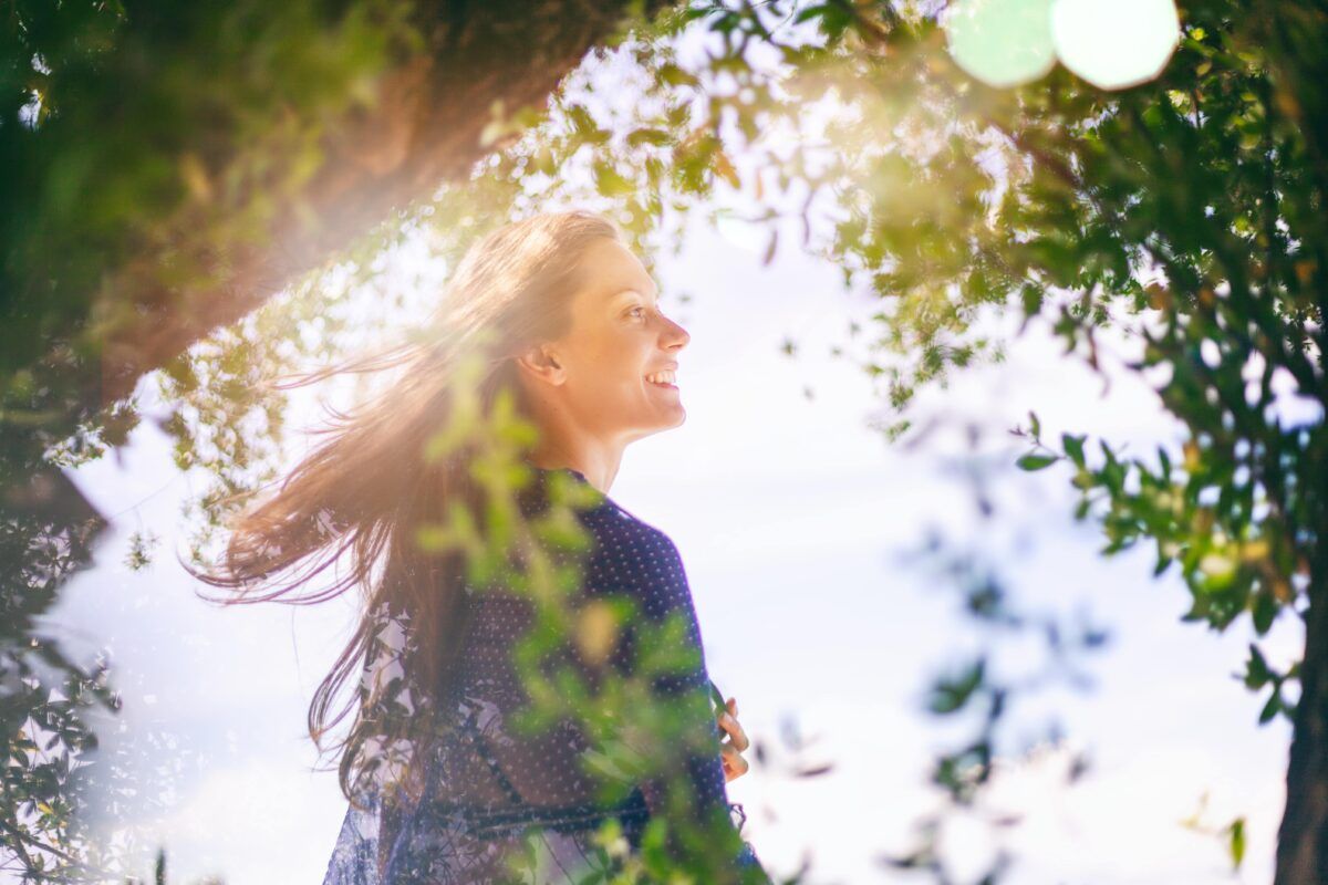 Beautiful happy young woman in green tree branches with glare from sun