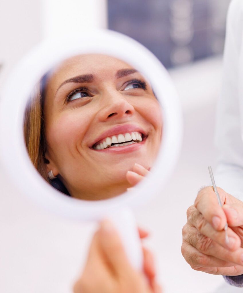 Woman looking in the mirror and smiling after dental checkup