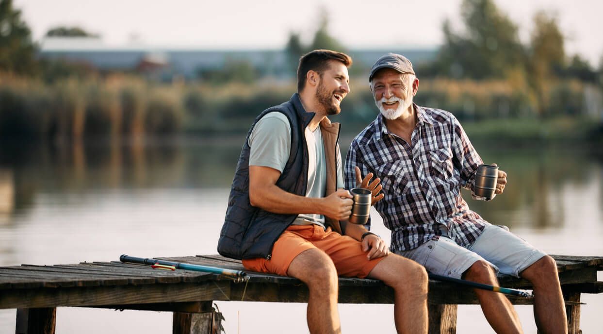 Happy senior fisherman and his adult son talking while having a drink