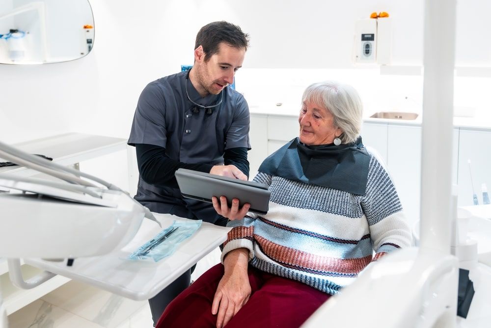 Dentist showing diagnosis and treatment plan on digital tablet to a senior woman patient during consultation in a modern dental clinic