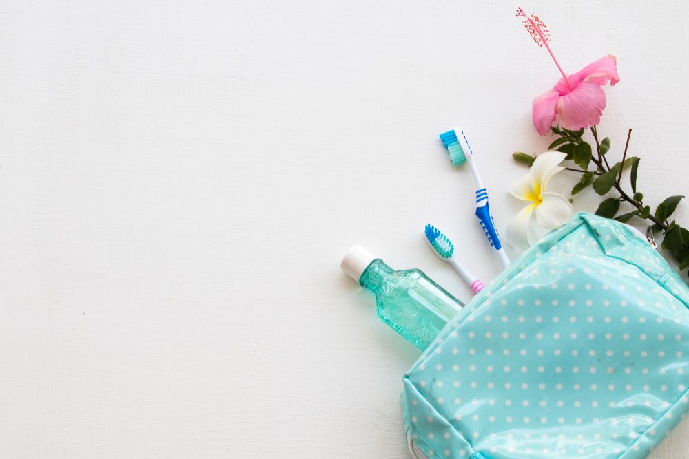 mouthwash ,toothbrush health care for oral cavity in blue bag travel with pink flower hibiscus on background white wood