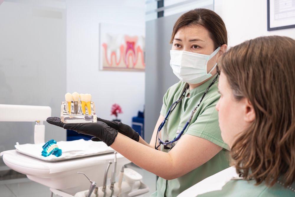Dental professional displaying a model of human teeth to a patient at a modern stomatology clinic, discussing dental implant procedures, the benefits of dental implants