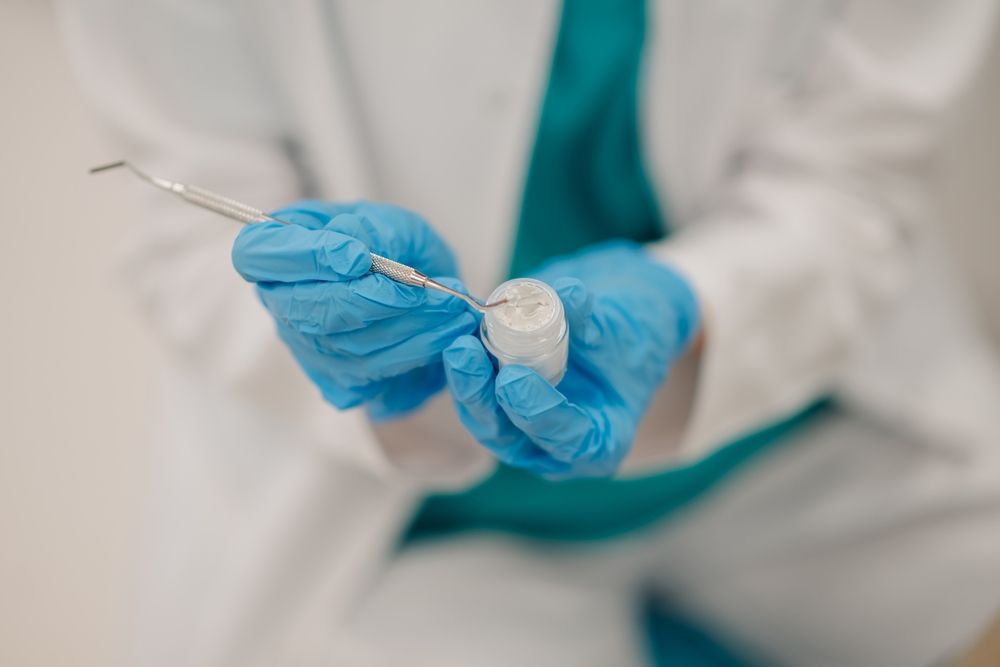 Dentist wearing blue gloves picking up dental filling material