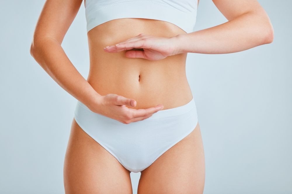 Hands, frame and stomach of woman in studio for liposuction, tummy tuck or plastic surgery. Weightloss results, underwear and slim female person with diet, gut health or fitness by white background.