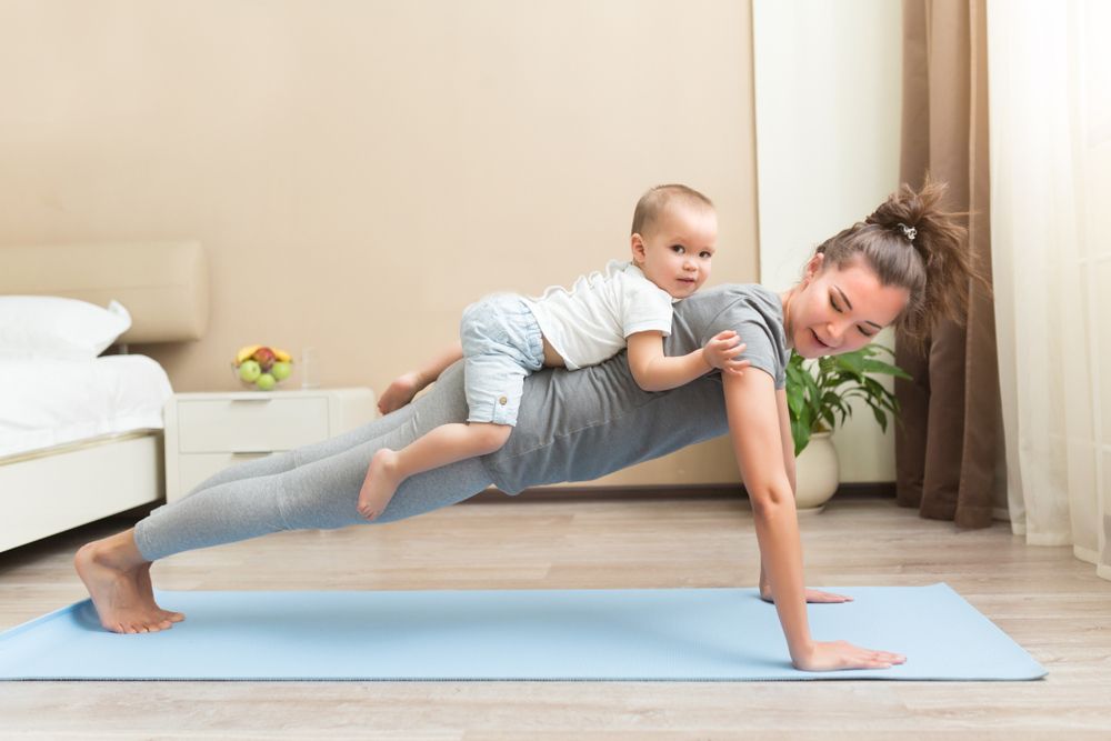 Happy young sporty pregnant mother doing physical yoga or pilates exercises together with her baby son at home