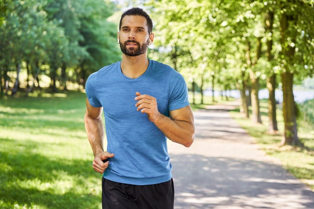 Active young man running with earphones in park during sunny day in spring summer