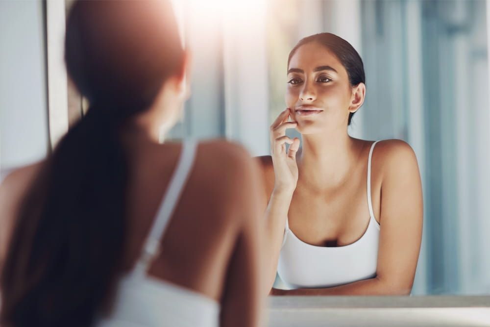 Woman, mirror and touch face in bathroom for skincare, results and beauty or cleaning.