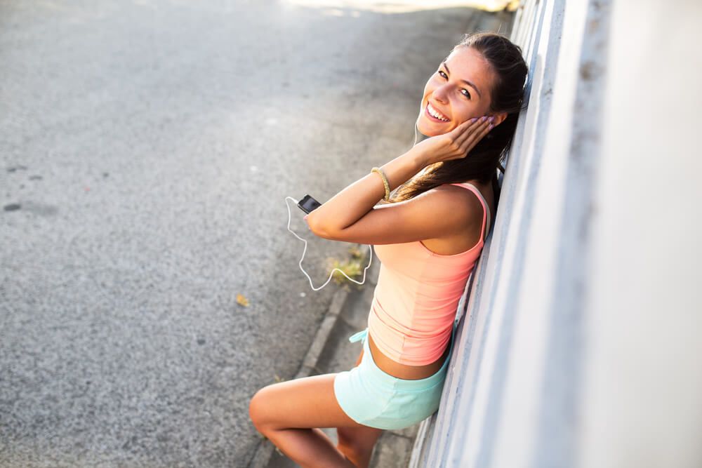 Young woman relaxing after jogging. using her smart phone and listening to music.