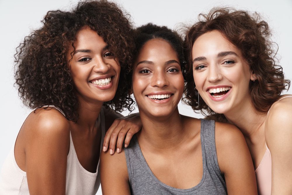 Portrait of three delighted multiracial women standing together and smiling
