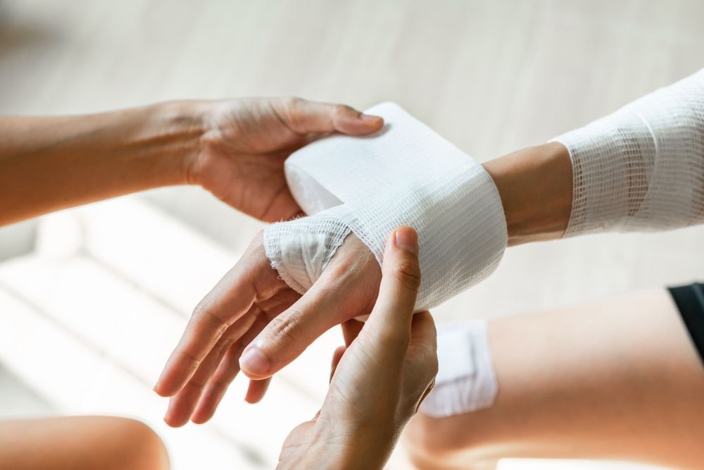 Sister wrapping her brother wrist and arm with bandage around injured hand at home