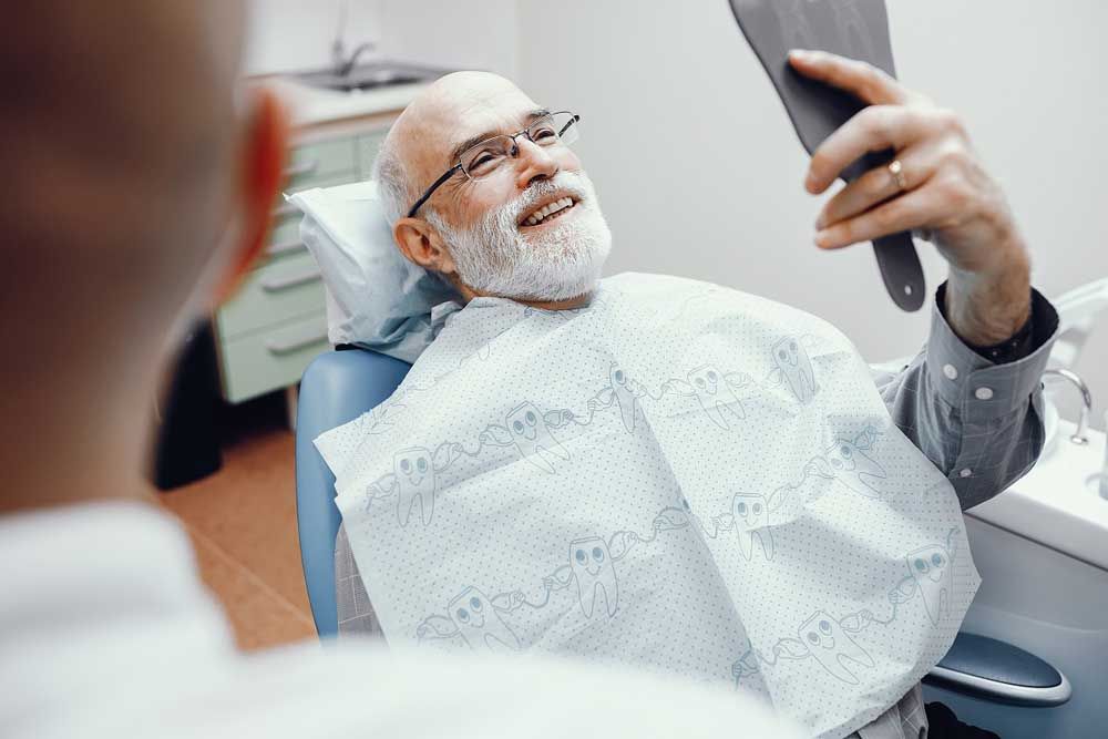 Aged man looking into the mirror on his teeth after treatment