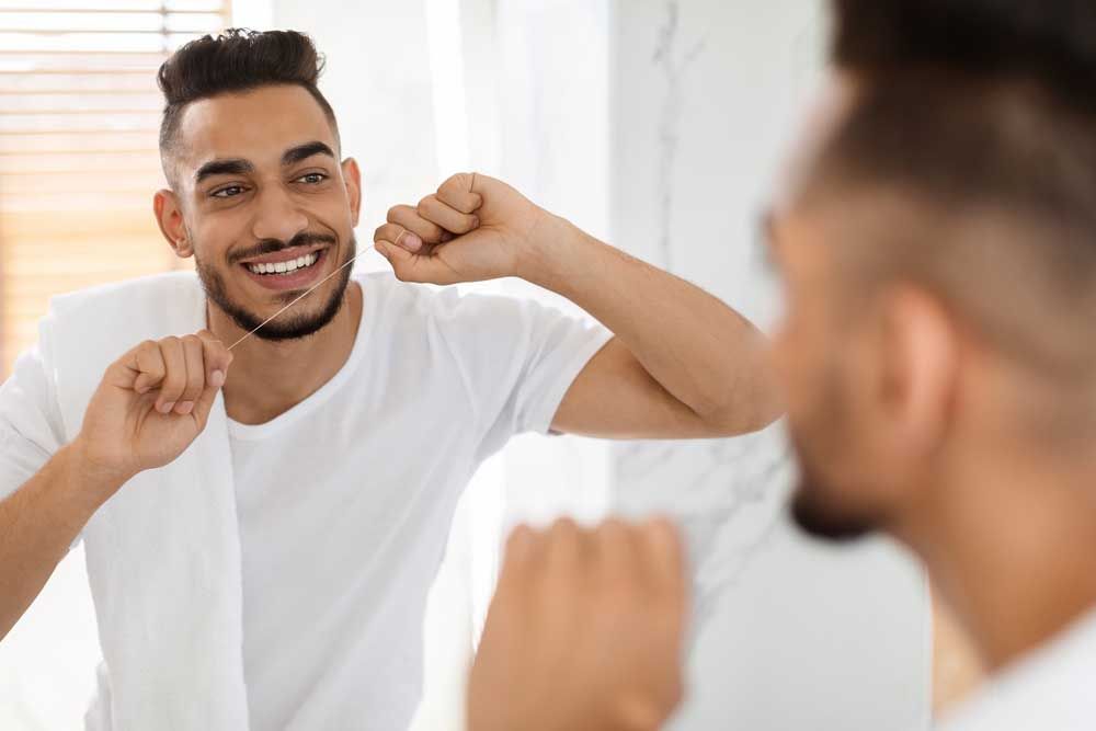 Smiling Man Using Dental Floss While Standing Near Mirror