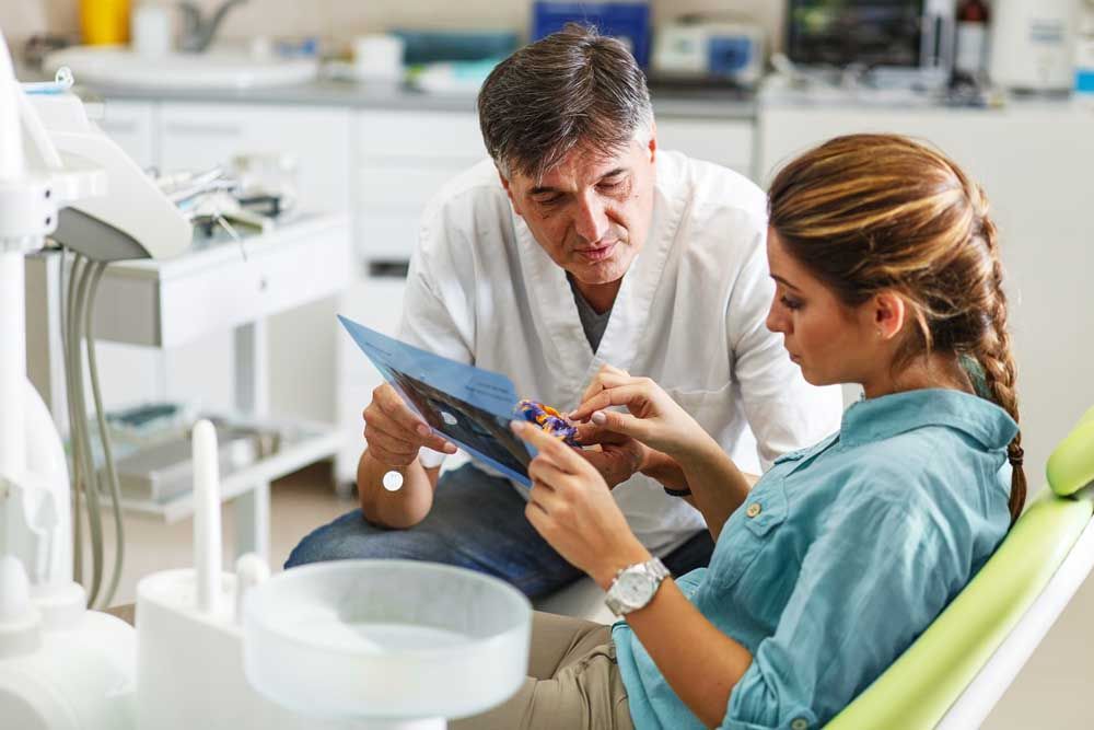 Senior male dentist in dental office talking with female patient