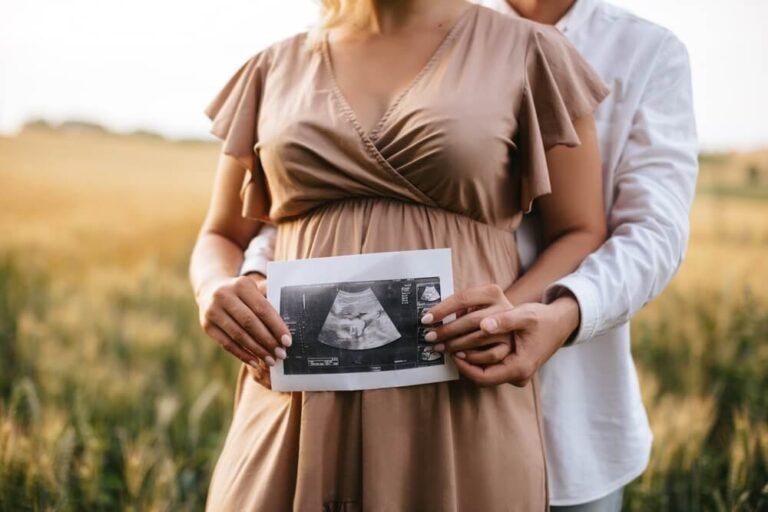 Pregnant woman with husband holding ultrasound baby image