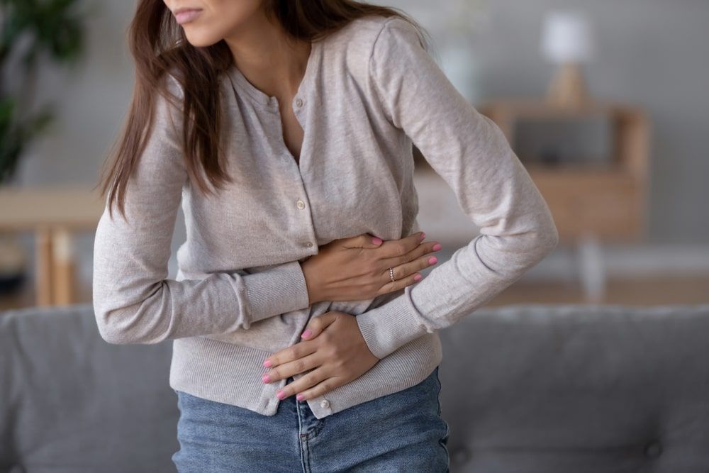 young sick woman standing holding belly suffering from stomach pain