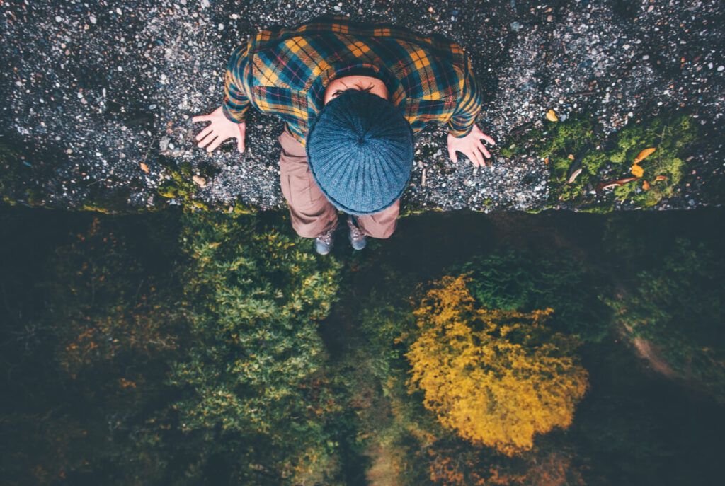 Man Traveler sitting on cliff bridge edge with forest aerial view