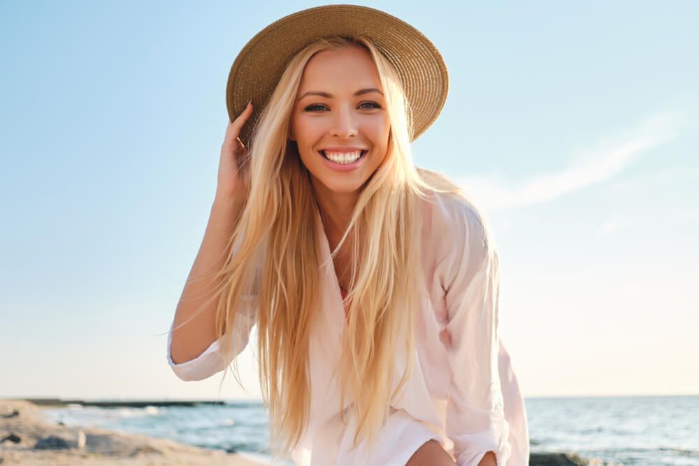 smiling woman in white shirt and hat at beach
