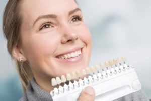 dentist using shade guide at woman's mouth to check veneer of teeth