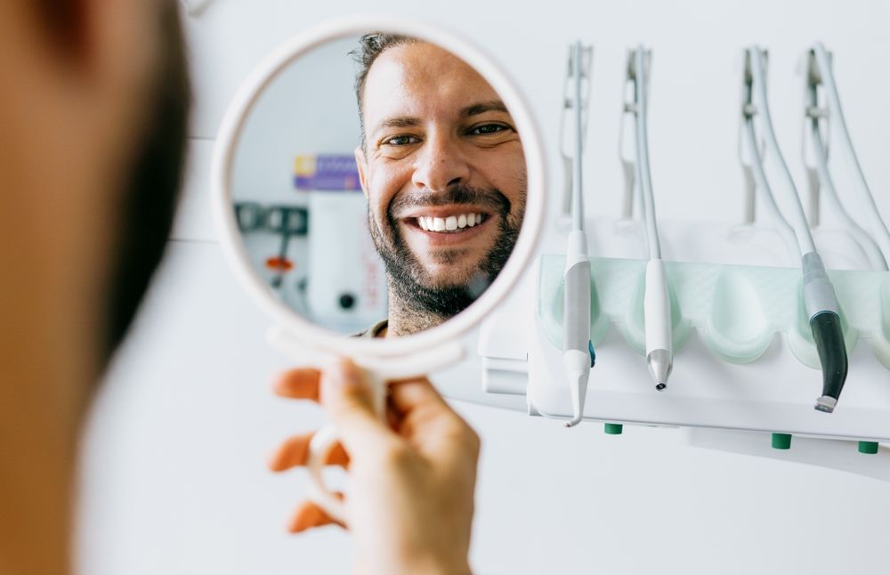 A man smiling in the mirror after receiving Cosmetic Dentistry