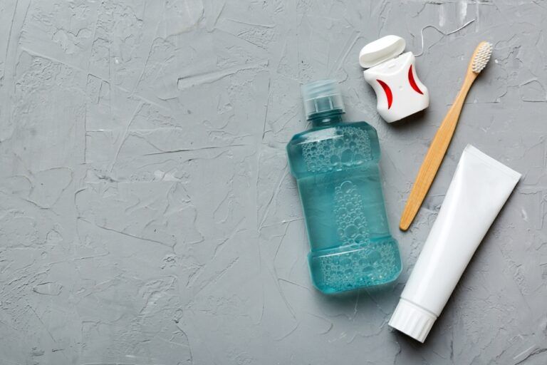 Mouthwash and other oral hygiene products on colored table