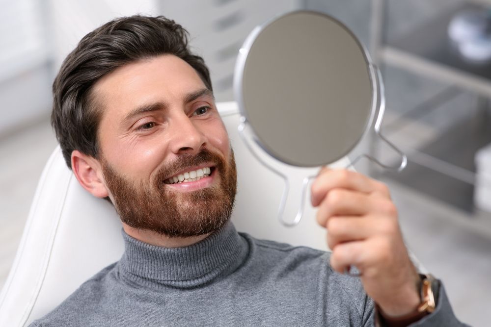 Man smiling in the mirror after receiving a Teeth Whitening treatment