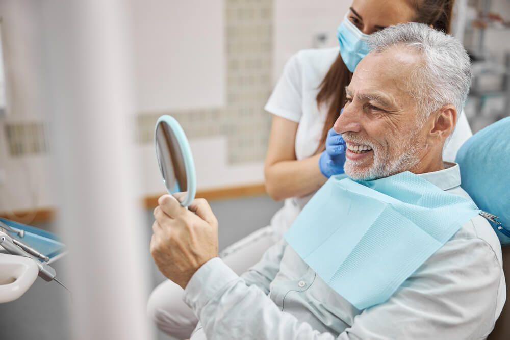 Joyous elderly man sitting in a dental chair while looking in the mirror