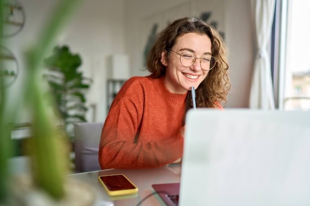 Happy young woman using laptop sitting at desk