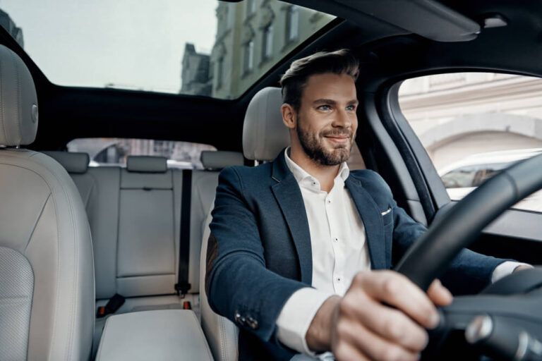 Handsome young man in full suit smiling while driving a car