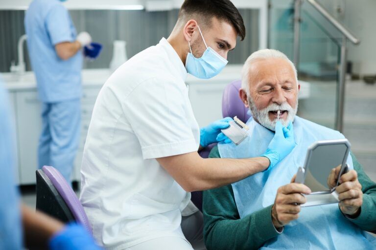 Young dentist and his senior patient choosing right shade of implants during dental appointment.