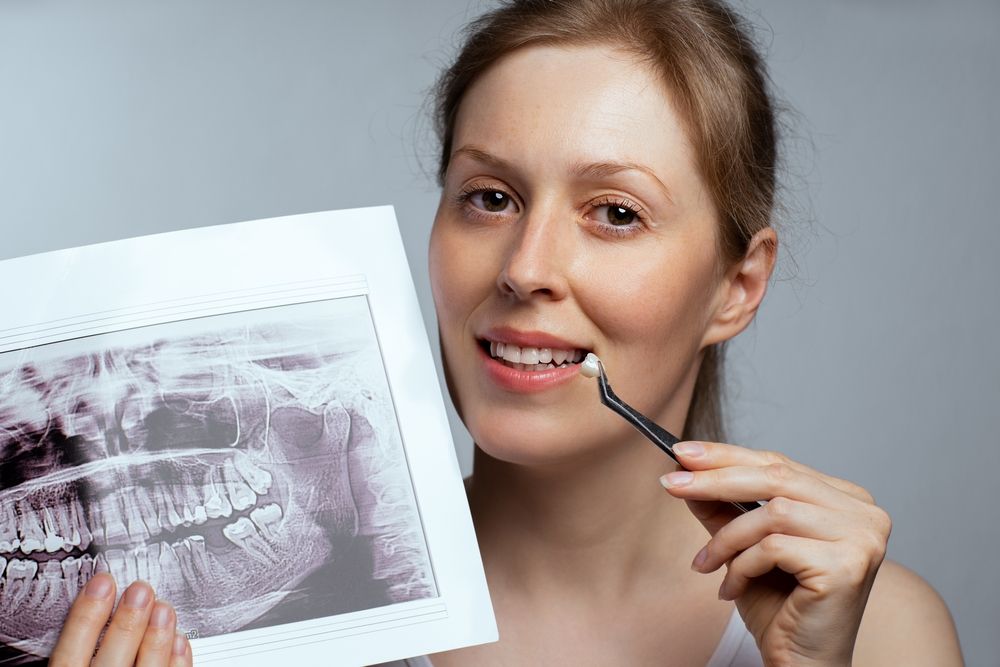 Portrait of young woman holding a dental crown and x-ray, dentistry concept