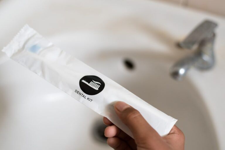 Hand holding a dental kit set against toilet wash basin. Concept of oral care, hygeine and travel