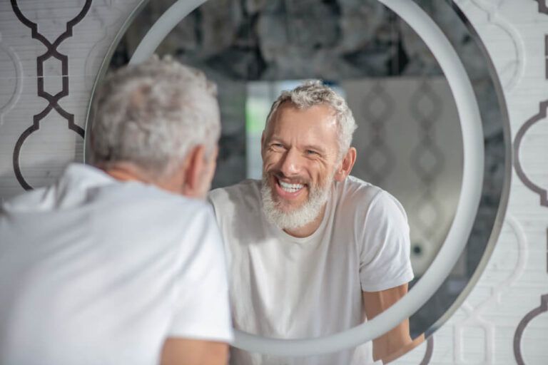 A smiling grey-haired man looking at the mirror