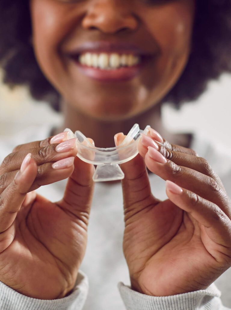 Happy, smiling young African American woman holding a teeth whitening tray