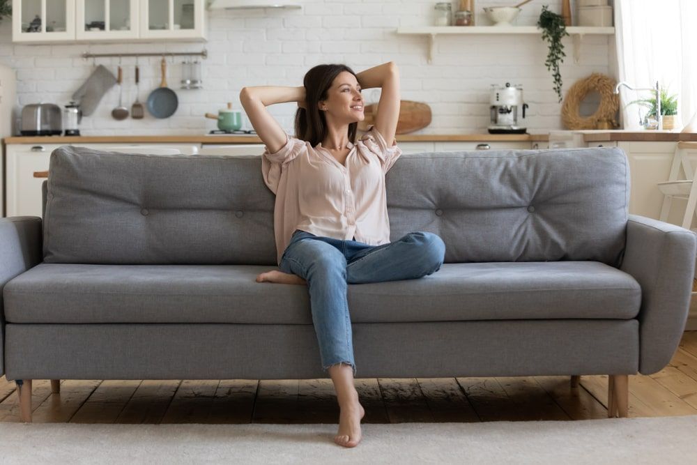 happy woman put hands behind head sitting leaned on couch
