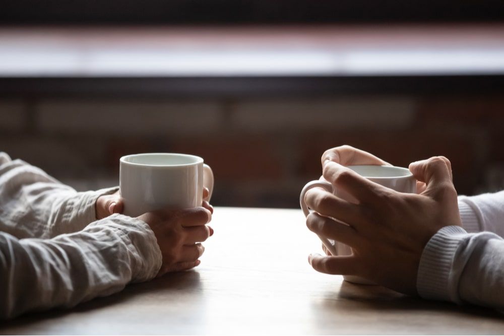 woman and man sitting in cafe, holding warm cups of coffee