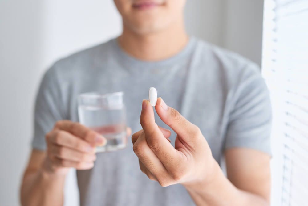 Happy asian man holding a pill and a glass of water looking at camera